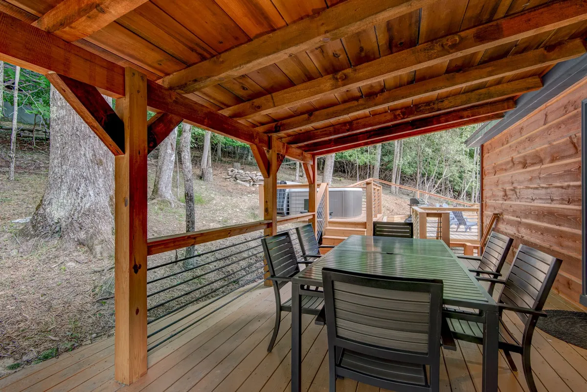 A spacious wooden deck with a dining table, bordered by sturdy railings and enveloped in trees. The space is ideal for outdoor dining, sunset drinks, or stargazing, providing direct access to the pristine surroundings.