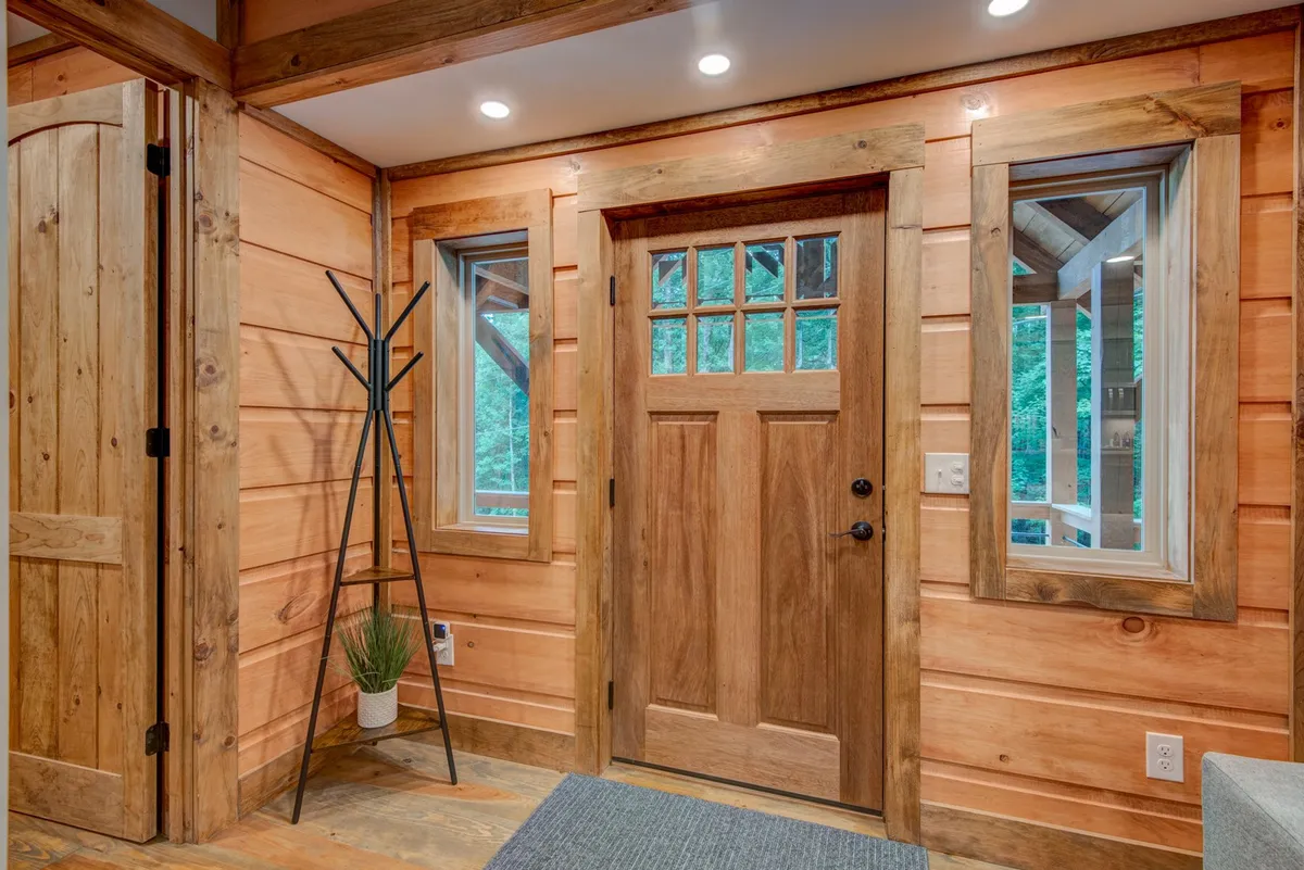 A welcoming entry/mudroom with a front door, windows, wood paneling, and a coat rack. The natural light and thoughtful design create an inviting first impression and a practical space for transitions.