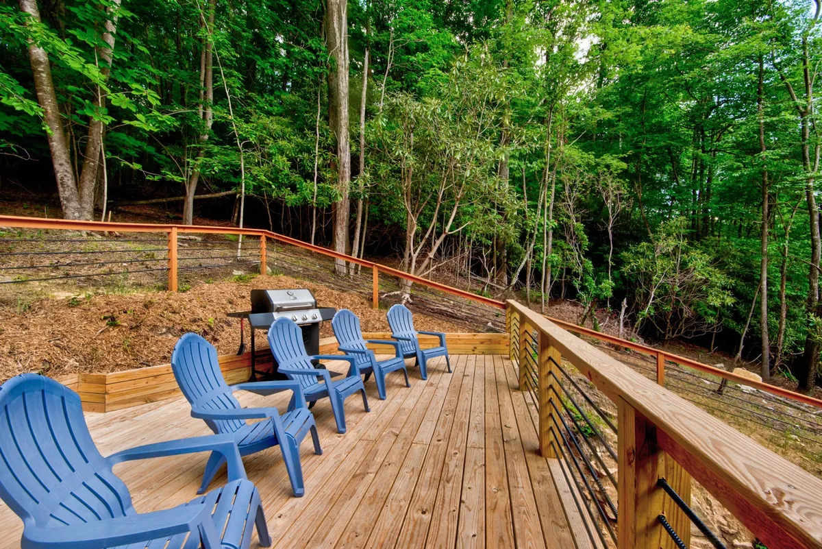 A deck area featuring comfortable chairs, a grill, and views of lush greenery, inviting guests to relax, barbecue, or gather with friends. The natural backdrop enhances the sense of being immersed in the outdoors.