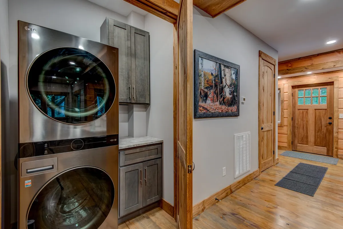 This image features a modern laundry area with stacked washer and dryer, wooden cabinetry, and an entrance door. The setting is both functional and inviting, reflecting the home's emphasis on practicality and comfort.