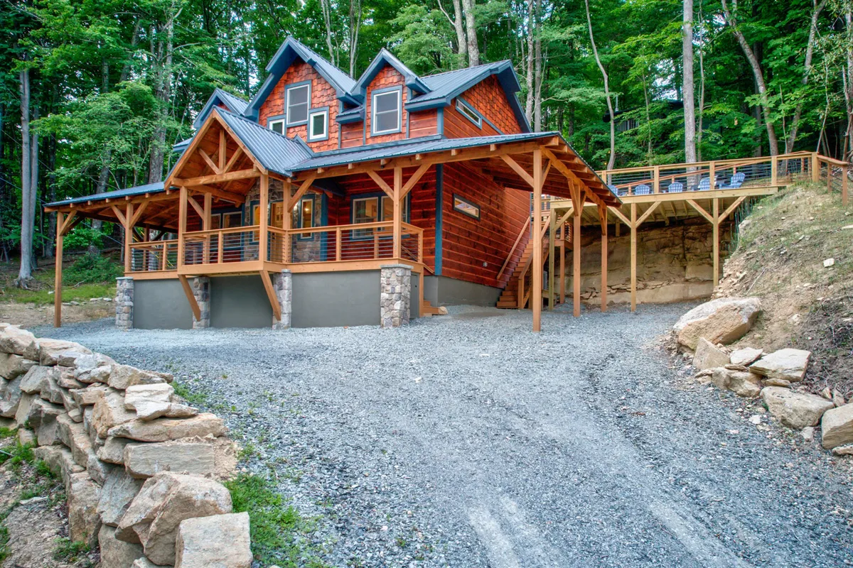 This image showcases the rustic cabin architecture of Pine Ridge Paradise, featuring a spacious wooden deck and stone accents. The surrounding trees and open yard create a welcoming, natural setting ideal for outdoor gatherings and group activities.