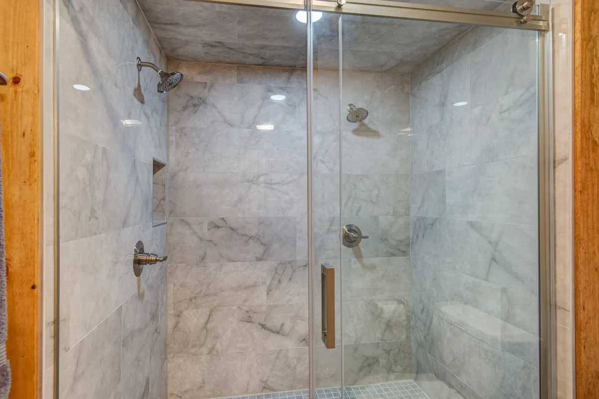 A contemporary bathroom featuring a glass shower enclosure, marble tile walls, and modern shower fixtures. The atmosphere is luxurious and rejuvenating, perfect for unwinding after a day of adventure.