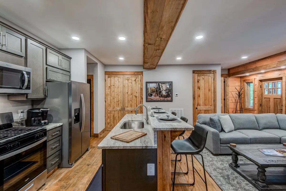 A modern, open kitchen with stylish appliances, wooden cabinetry, a comfortable sofa, and bar stools. The ambiance is cozy and inviting, perfect for gatherings and relaxing with family.