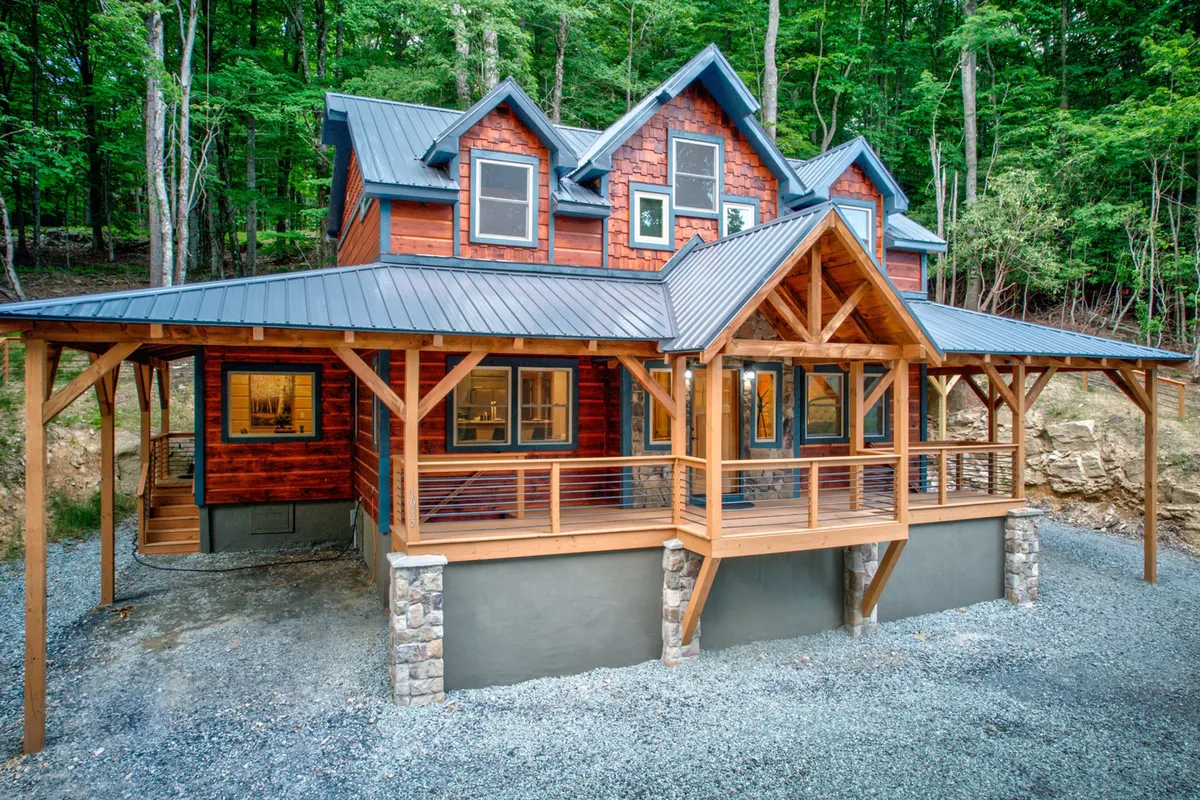 The image showcases the inviting exterior of a newly built mountain cabin, featuring a spacious front porch with sturdy wooden beams, a charming stone foundation, and expansive windows that offer breathtaking views. The setting exudes warmth and welcome, hinting at memorable outdoor gatherings, quiet mornings with coffee, and evenings spent watching sunsets amidst the tranquility of Beech Mountain.